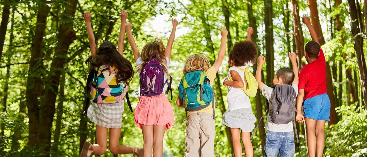 Gruppe Kinder mit Rucksäcken in der Natur im Sommer springt in die Luft