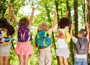 Gruppe Kinder mit Rucksäcken in der Natur im Sommer springt in die Luft