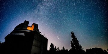 Blick auf eine Sternwarte vor einem sternenbehangenen Nachthimmel