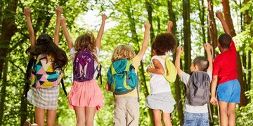 Gruppe Kinder mit Rucksäcken in der Natur im Sommer springt in die Luft