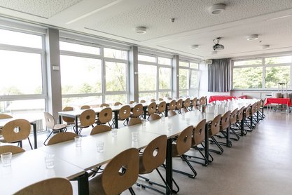 Raum mit Glasfront in dem eine lange Tischreihe mit Stühlen aufgestellt ist  