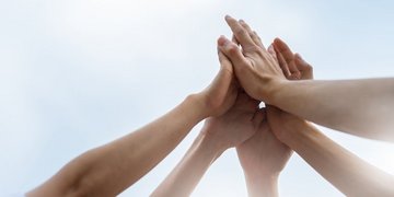 Mehrere Menschen klatschen sich gemeinsam vor blauem Himmel ab