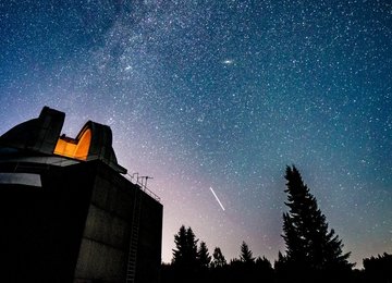 Blick auf eine Sternwarte vor einem sternenbehangenen Nachthimmel